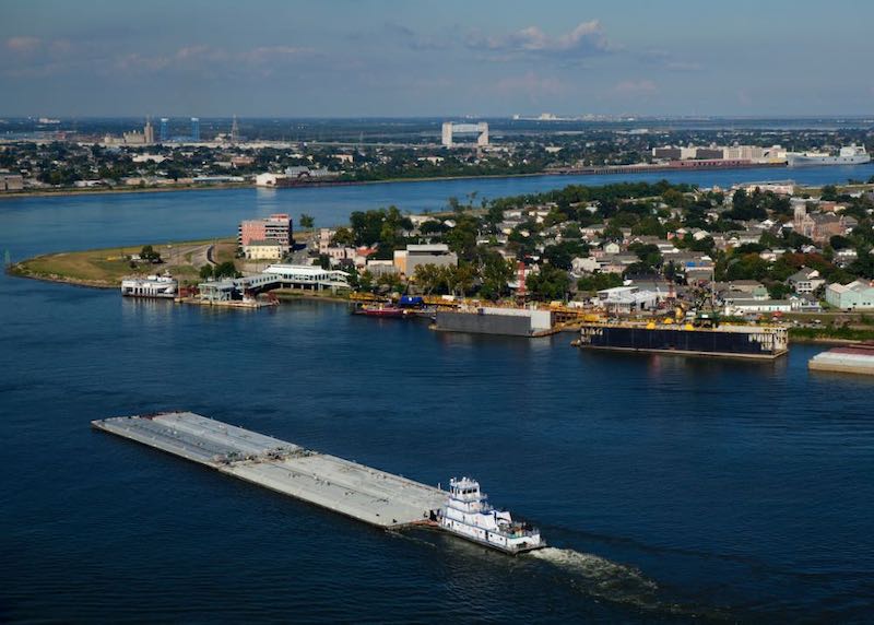 Tug pushing a barge going around Algiers Point on the Mississippi River with the Bywater neighborhood behind.